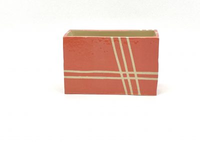 Mit der Plattentechnik hergestellte Keramik. Eine rote Box mit weißen geometrisch verteilten Streifen in Prismaform mit rechteckigem Grundriss.