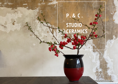 Vase in Dunkelbraun und Rot mit einem Ast und dunkelroten Blüten und darüber das Logo vom Ceramic-Studio P. & C. STUDIO CERAMICS.
