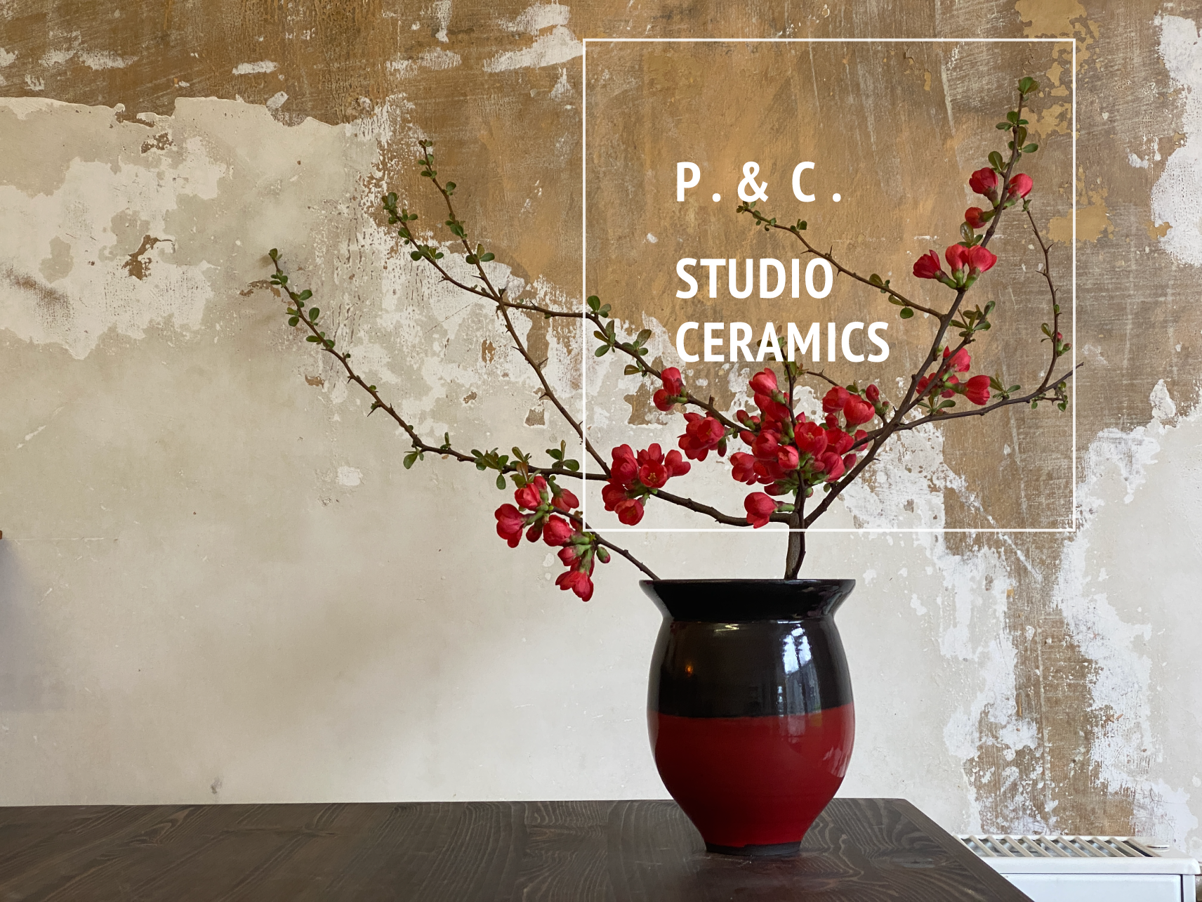 Vase in Dunkelbraun und Rot mit einem Ast und dunkelroten Blüten und darüber das Logo vom Ceramic-Studio P. & C. STUDIO CERAMICS.